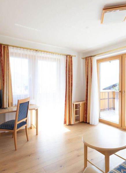 Wohnzimmer mit Schreibtisch, Fernseher und Balkon der Hirzer Suite